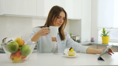 Mutfakta kahve içme ve bir tablet bilgisayar kullanarak oldukça genç bayan