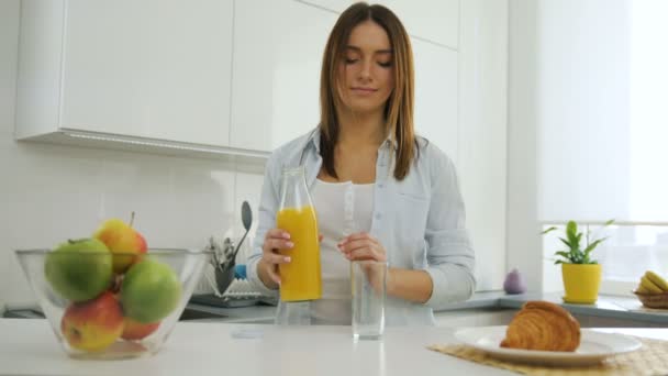 Hübsche junge Frau in der Küche, die sich ein Glas Orangensaft einschenkt. — Stockvideo