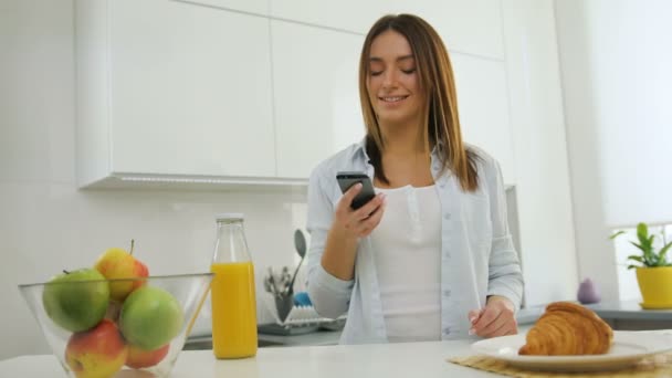 Mujer bastante joven en la cocina llamando a su amigo usando un teléfono inteligente — Vídeo de stock