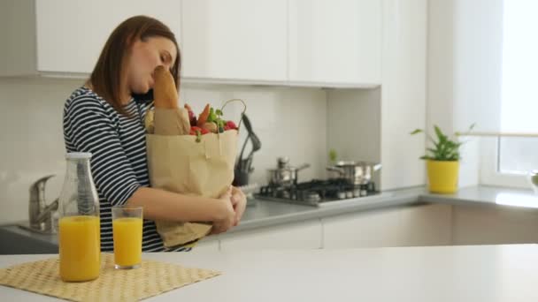 年轻女子回来回家后购物，用智能手机通话 — 图库视频影像