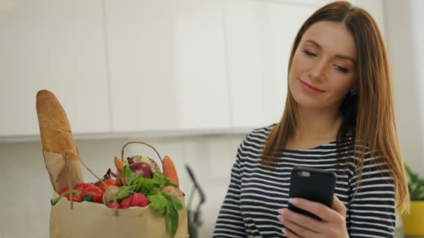 Vrouw kwam terug naar huis van boodschappen texting op haar mobiel — Stockvideo