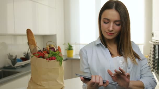 Woman scrolling through her files on her tablet computer in the kitchen. — Stock Video