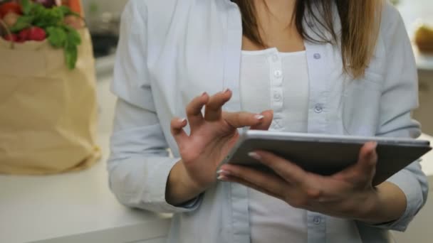 Vrouw scrollen door haar bestanden op haar tablet-pc in de keuken. — Stockvideo