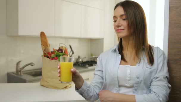 Mulher bebendo suco de laranja na cozinha. — Vídeo de Stock