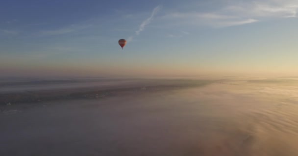 Hete luchtballon zwevend in de zuivere blauwe hemel op de zonsopgang boven de stad — Stockvideo