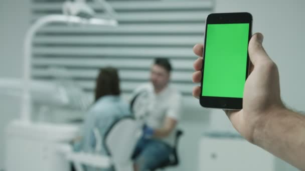 Slimme telefoon met groen scherm, op achtergrond van werkende tandarts en patient. — Stockvideo