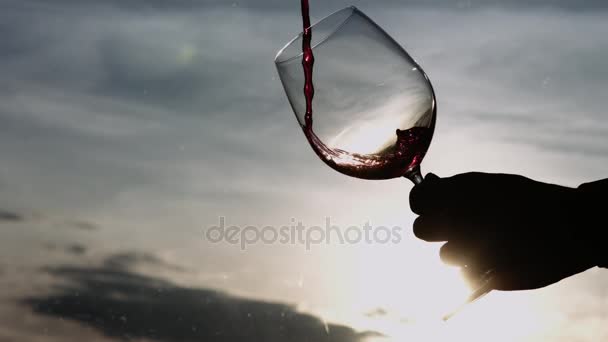 Mano sosteniendo el vaso que se llena lentamente con vino tinto — Vídeos de Stock