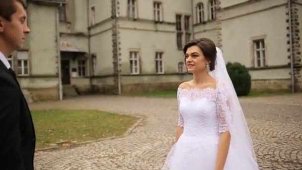 Красивая невеста идет к жениху, обнимает его на открытом воздухе возле античного замка — стоковое видео