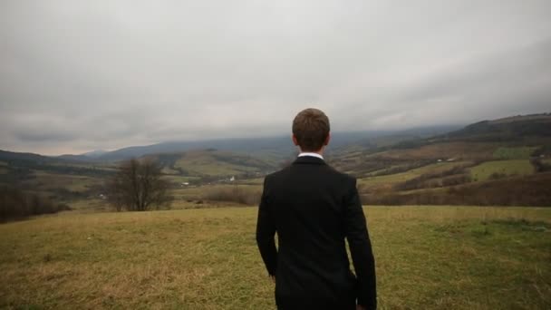 Vista trasera cercana del novio caminando en la colina de la montaña — Vídeos de Stock