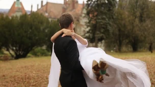 Bräutigam schwingt Braut auf Händen nahe altem Schloss — Stockvideo