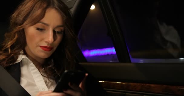 Mujer de negocios monta en el asiento trasero del coche y mensajes de texto en el teléfono inteligente — Vídeos de Stock