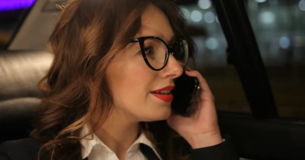 Женщина в машине разговаривает по телефону. На заднем плане ночные городские здания, автомобили, лигатуры — стоковое видео