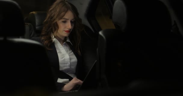 Atractiva mujer de negocios trabaja en un ordenador portátil en el asiento trasero del coche — Vídeos de Stock
