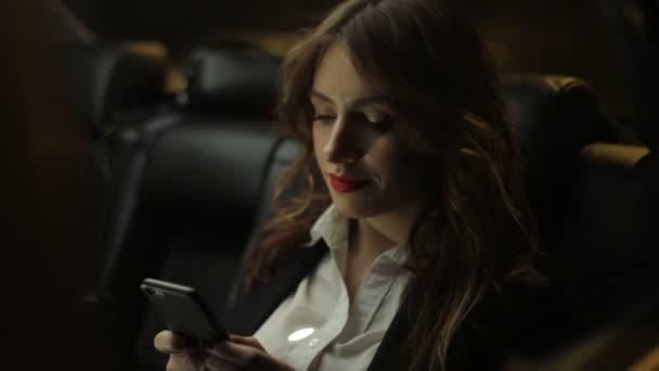 Encantadora mujer cabalga en el asiento trasero del coche escribiendo y hablando en el teléfono móvil — Vídeos de Stock