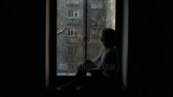 Sylwetka kobiety siedząc na parapecie i patrząc przez okno — Wideo stockowe