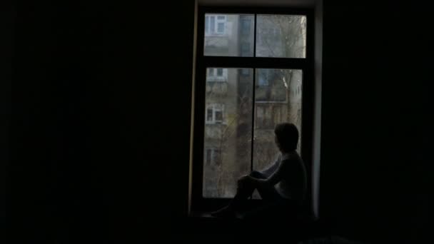 Pervazın üzerinde oturan ve pencereden dışarı bakarak bir kadın silüeti — Stok video
