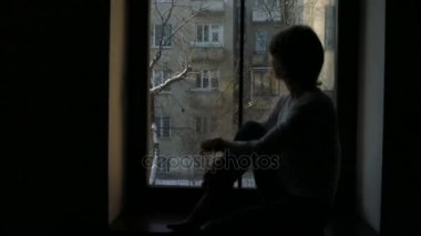 Kadın pencere kenarında oturan ve yürekli kırık pencereden dışarı bakarak