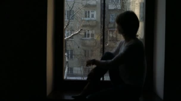 Female sitting on the windowsill and looking out the window, broken hearted — Stock Video