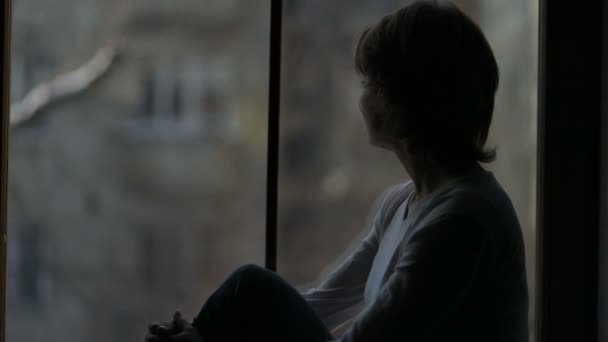 Καταθλιπτική γυναίκα κάθεται στο περβάζι του και κοιτάζοντας έξω από το παράθυρο, καρδιαλγής — Αρχείο Βίντεο