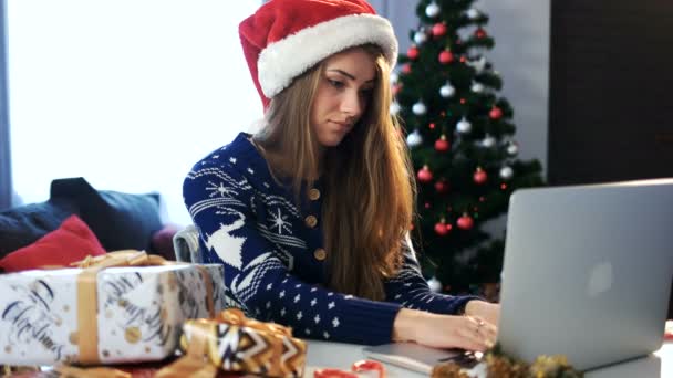 圣诞老人的帽子在笔记本上工作的女孩。圣诞晚会和快乐新的一年 — 图库视频影像