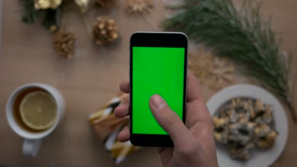 Mans hand met behulp van slimme telefoon met groen scherm op hout achtergrond met kerstcadeau en de cookies. Bovenaanzicht. Chromakey. — Stockvideo