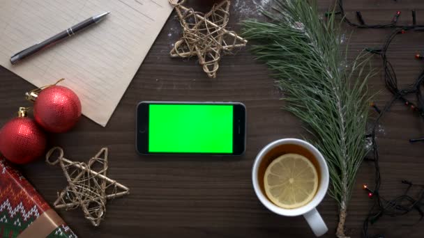 Mans hand söka något i smart telefon med grön skärm på brunt trä bakgrund med juldekoration. Ovanifrån. Färgtransparens. Horisontellt läge. — Stockvideo