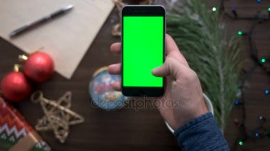 Bir şey çay, yıldız, oyuncak ve garland kahverengi ahşap zemin üzerine yeşil ekranlı akıllı telefon arama el mans. Üstten Görünüm. Chroma anahtar.
