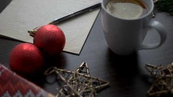 Té de Navidad con juguetes rojos, estrellas, bolígrafo y cuaderno sobre mesa de madera marrón. Decoración de Navidad. Vista superior . — Vídeos de Stock
