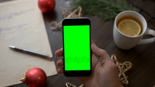 Slimme telefoon met groen scherm op bruin houten tafel met kerst decoratie en nota boek. Bovenaanzicht. Chromakey. — Stockvideo