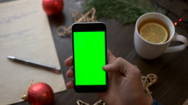 Man handen met behulp van slimme telefoon met groen scherm op bruin houten tafel met kerst decoratie en nota boek. Bovenaanzicht. Chromakey. — Stockvideo