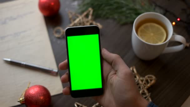 Slimme telefoon met groen scherm op bruin houten tafel met kerst decoratie en nota boek. Bovenaanzicht. Chromakey. — Stockvideo