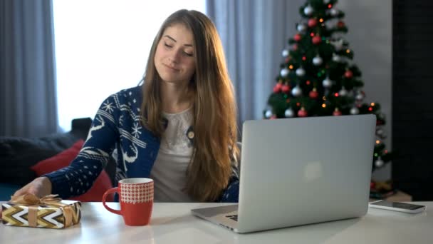 Mosolygó fiatal nő laptop gépelés a nappaliban a karácsonyfa háttér. — Stock videók