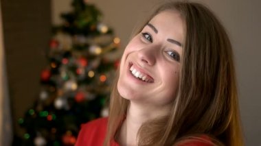 Poz ve Noel ağacı arka plan üzerinde fotoğraf makinesinde gülümseyen şık kazaklı genç kadın.