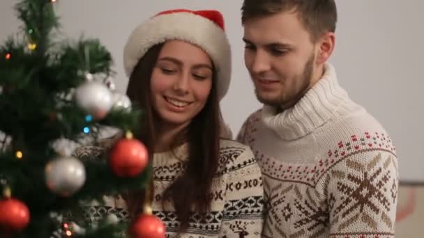 Feliz joven pareja divirtiéndose, sonriendo y hablando cerca del árbol de Navidad en suéteres elegantes . — Vídeos de Stock