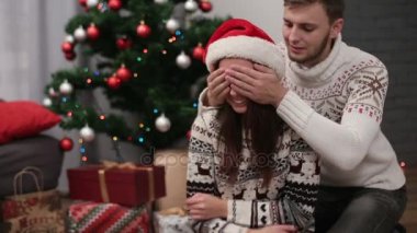 Kadının gözlerini kapatma ve burada Noel ağacı arka plan üzerinde Noel Hediye veren genç çekici adam.