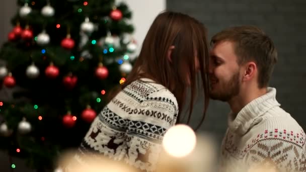 Atractivo hombre y mujer feliz abrazándose en el fondo del árbol de Navidad. Pareja joven enamorada celebrando el Año Nuevo. De cerca. De interior . — Vídeos de Stock