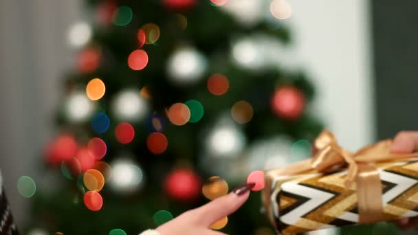 五彩缤纷的礼品给女朋友上与指示灯闪烁的圣诞树背景的年轻男人的手。关闭. — 图库视频影像