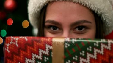 Bir Noel hediyesi tutan genç çekici kadın portresi gözler yakın ve christmastree arka plan, kameraya gülümseyen yakın çekim.