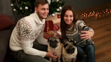 Mutlu genç çift gülümseyen ve selfie pug köpek Noel ağacı yakınındaki birkaç ile yapım seviyorum. Üstten Görünüm.