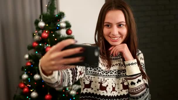 Attraktive junge Frau beim Selfie auf dem Smartphone mit Weihnachtsbaum im Pullover mit Hirsch. Nahaufnahme. — Stockvideo