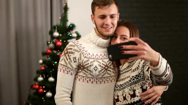 Heureux jeune homme et femme étreignant et prenant selfie sur téléphone intelligent sur fond d'arbre de Noël . — Video