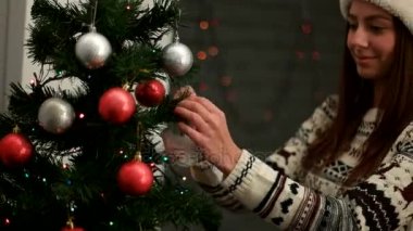 Bir Noel ağacı kırmızı ve gümüş oyuncak dekorasyon santa claus şapka genç çekici kadın. Yakın çekim.