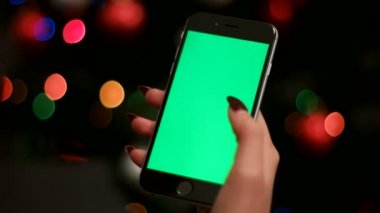 Kadın el çelenk bokeh arka plan üzerinde yeşil ekranlı akıllı telefon kullanarak. Yakın çekim. Chroma anahtar.