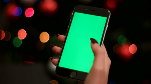 Main de femme en utilisant un téléphone intelligent avec écran vert sur fond de guirlandes bokeh. Ferme là. Clé chromatique . — Video