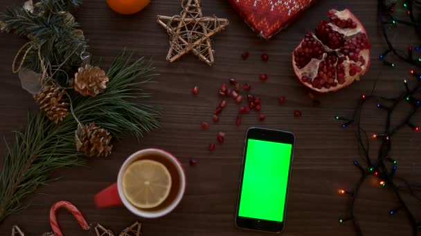Maschio dito toccando su uno smart phone touchscreen con schermo verde. Arredo natalizio sullo sfondo del tavolo in legno. Chiave cromatica. Vista dall'alto, Colpito dall'alto — Video Stock