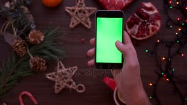 Üstten Görünüm adam akıllı telefon ile yeşil ekran kullanarak ele. Dokunarak ve Noel masa artalanını dokunmatik ekran sayfalarında kaydırma parmak. Chroma anahtar. Yukarıdan görüntülemek
