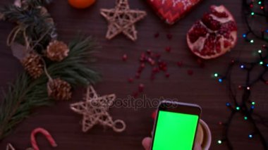 Noel üstten görünüm. Akıllı telefon ile yeşil ekran kullanarak adam ele. Parmak dokunmatik ekran sayfalarında tomar. Ahşap masa arka plan Christmas ayrıntılar. Chroma anahtar. Yukarıdan görüntülemek