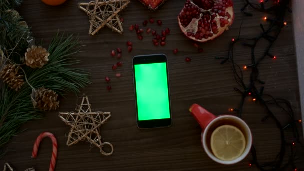 Mano del hombre vista superior utilizando el teléfono inteligente con pantalla verde. Páginas de desplazamiento del dedo en la pantalla táctil. Detalles de Navidad sobre fondo de mesa de madera. Clave de croma — Vídeos de Stock