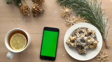 Noel üstten görünüm. Ahşap masa üstünde yeşil perde ile akıllı telefon. Noel dekorasyonu, bisküvi, çay. Chroma anahtar