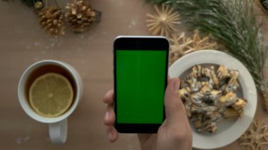 Üstten Görünüm adam elini tutarak akıllı telefon yeşil ekran ile. Dokunarak ve Noel masa artalanını dokunmatik ekran sayfalarında kaydırma parmak. Chroma anahtar